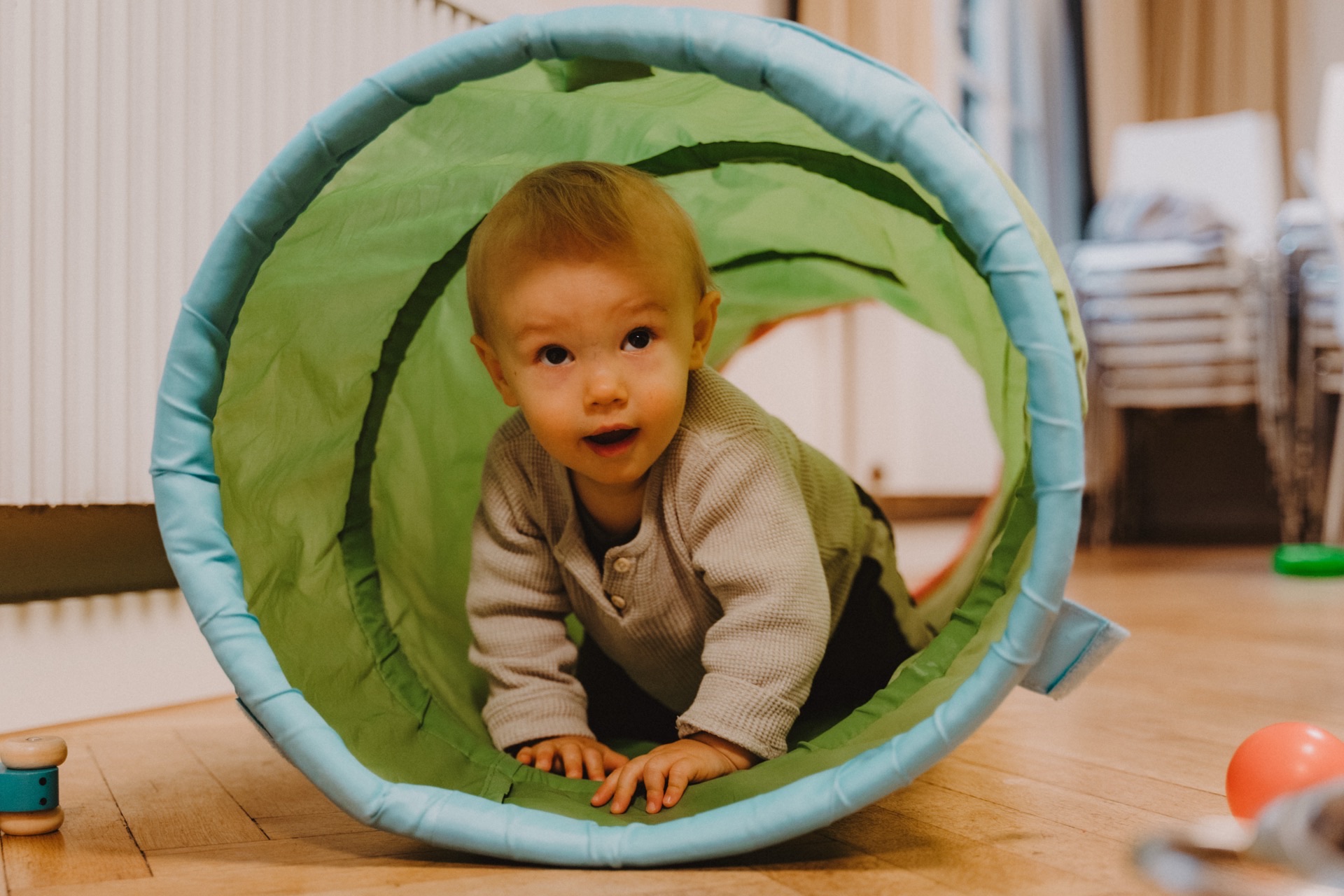 Baby krabbelt durch grünen Spieltunnel im Wohnzimmer