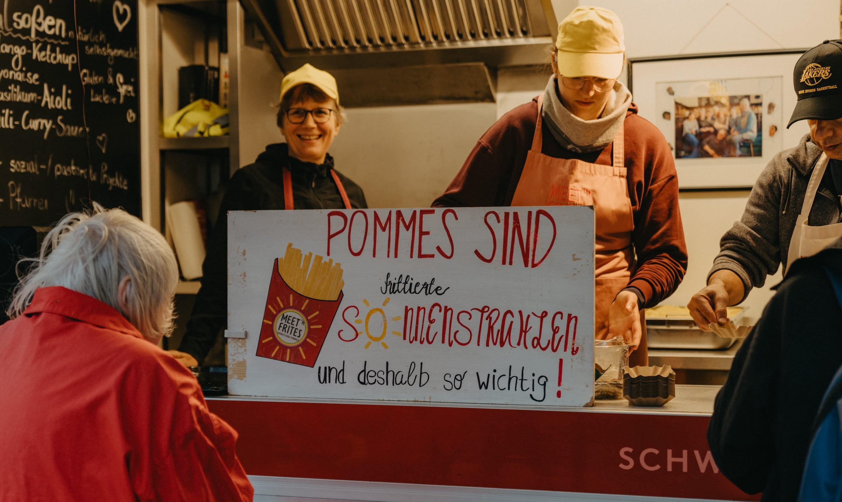 Imbissstand mit Pommes-Schild und Verkäufern