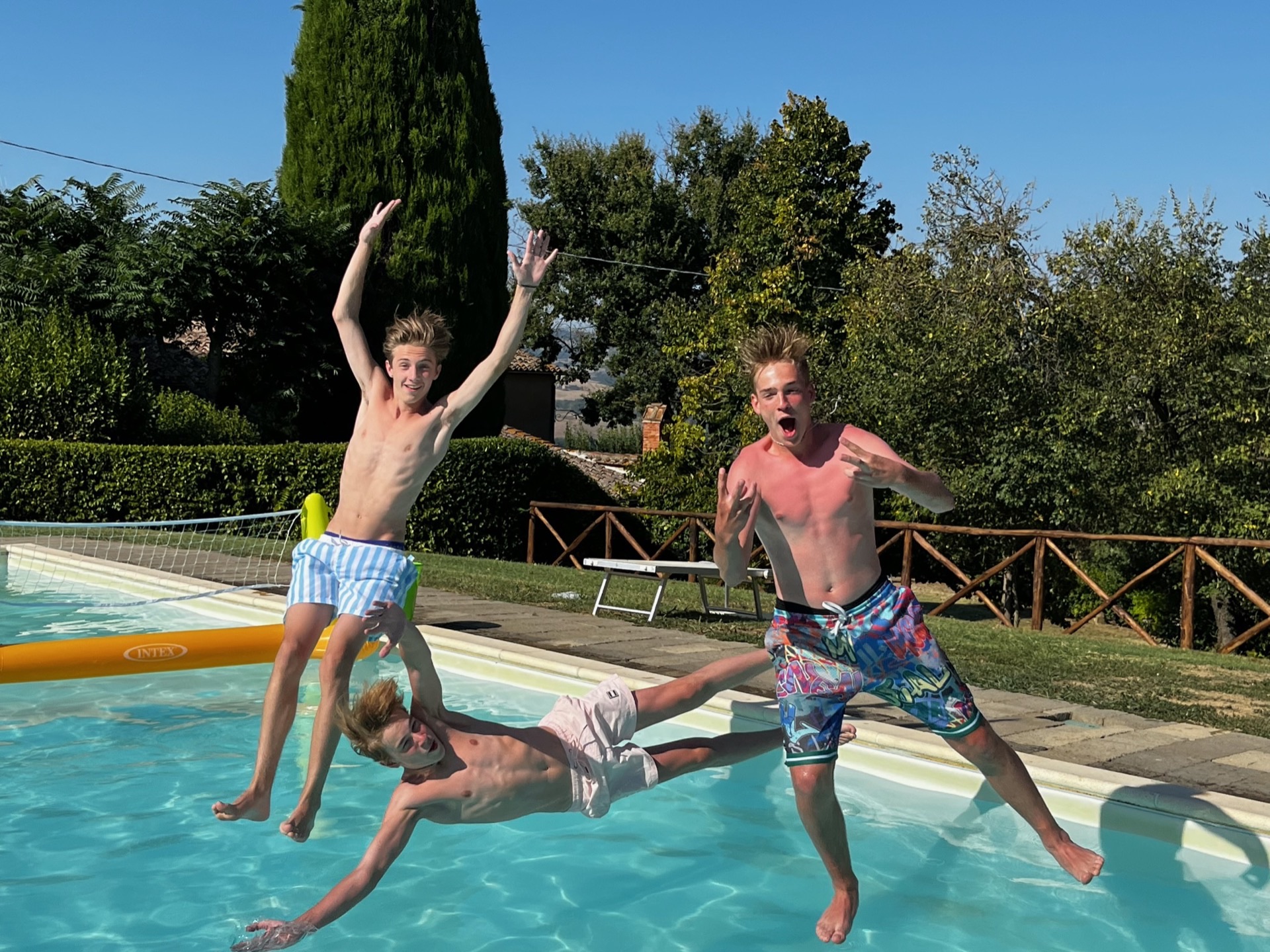 Drei Jugendliche springen lachend in einen Pool